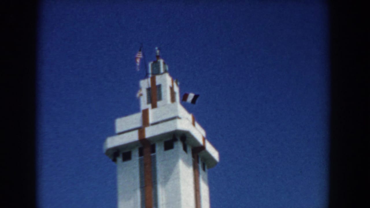 White tower top with two flags and a dark pennant in the sky.