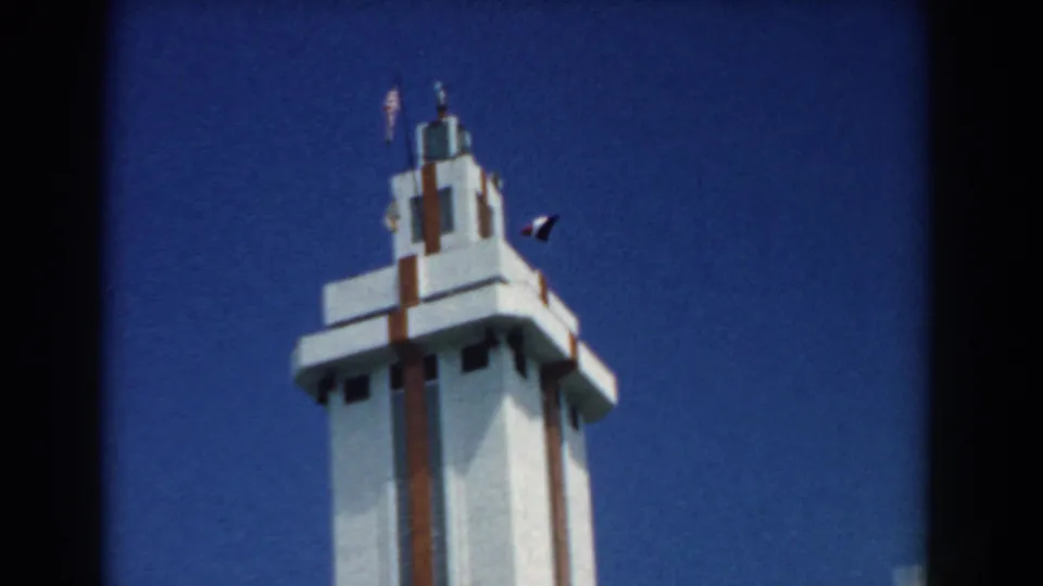 A slightly wider 8mm view shows the white and red tower top with flags fluttering above, set against clear blue sky.