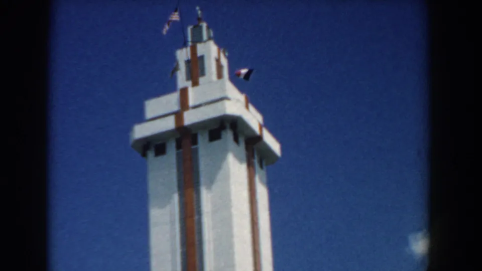The final frame shows the tower top shifted right, with flags and a dark wind marker still visible against the saturated blue sky.