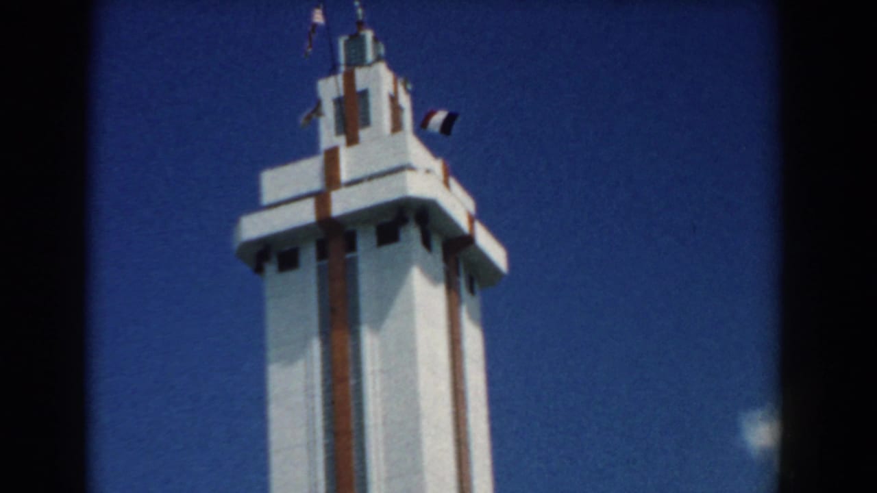 Tall white tower with brown vertical trim and small flags against a blue sky.