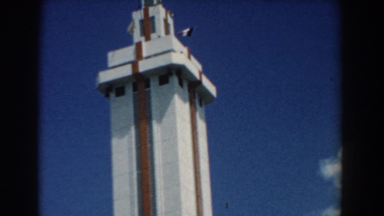 Upper portion of a white tower with flags near the roofline under a clear sky.