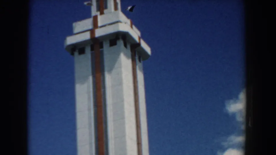 1958 South Carolina 8mm still showing a tall white tower with brown trim, small flag detail and clouds near the frame edge.