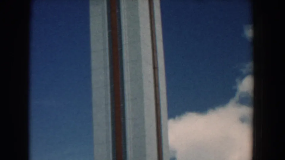 Handheld 1958 home-movie frame showing the striped tower continuing upward beside a large white cloud.