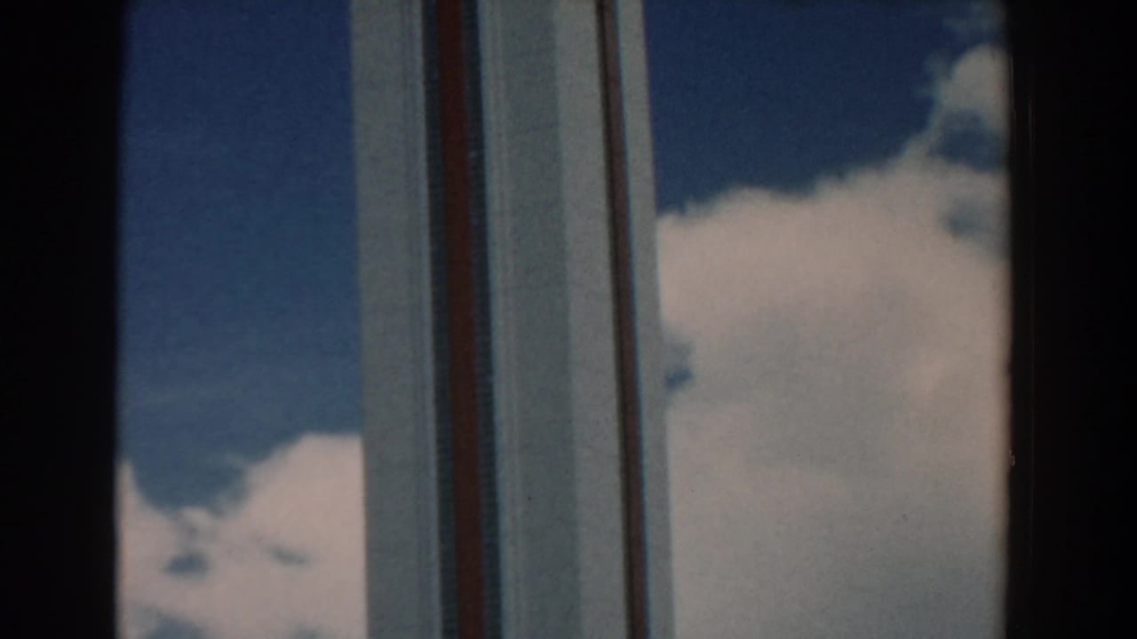 Vertical bands of a tall facade appear between dark foreground window frames and clouds.