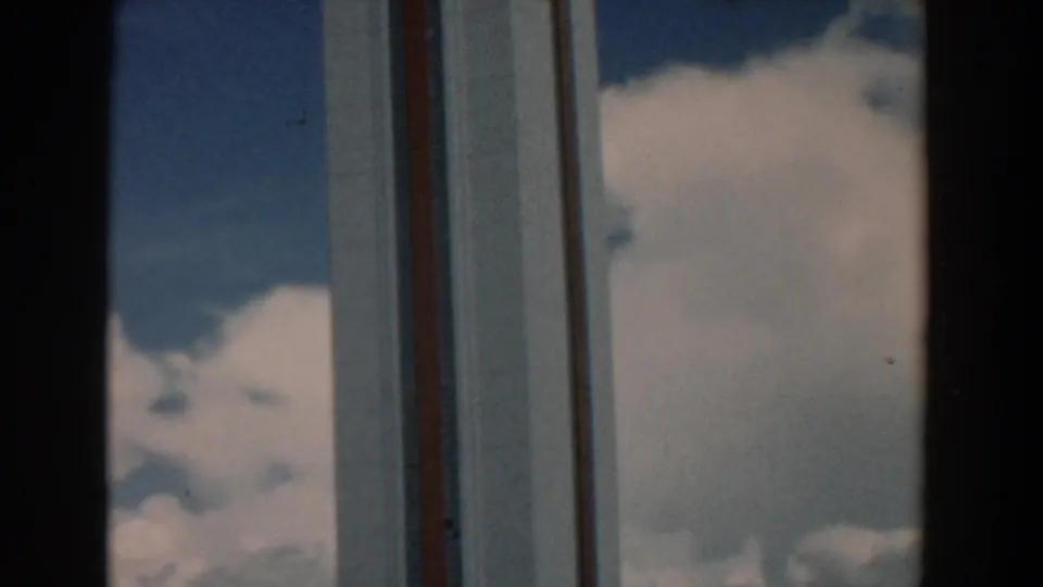 1958 South Carolina 8mm frame showing clouds and a modern building facade through dark window-like vertical framing.