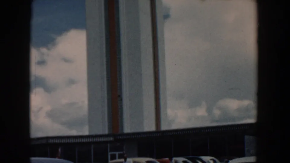 1958 South Carolina 8mm frame with a tall striped building facade, dark window framing, clouds, and a small lower edge of structure.