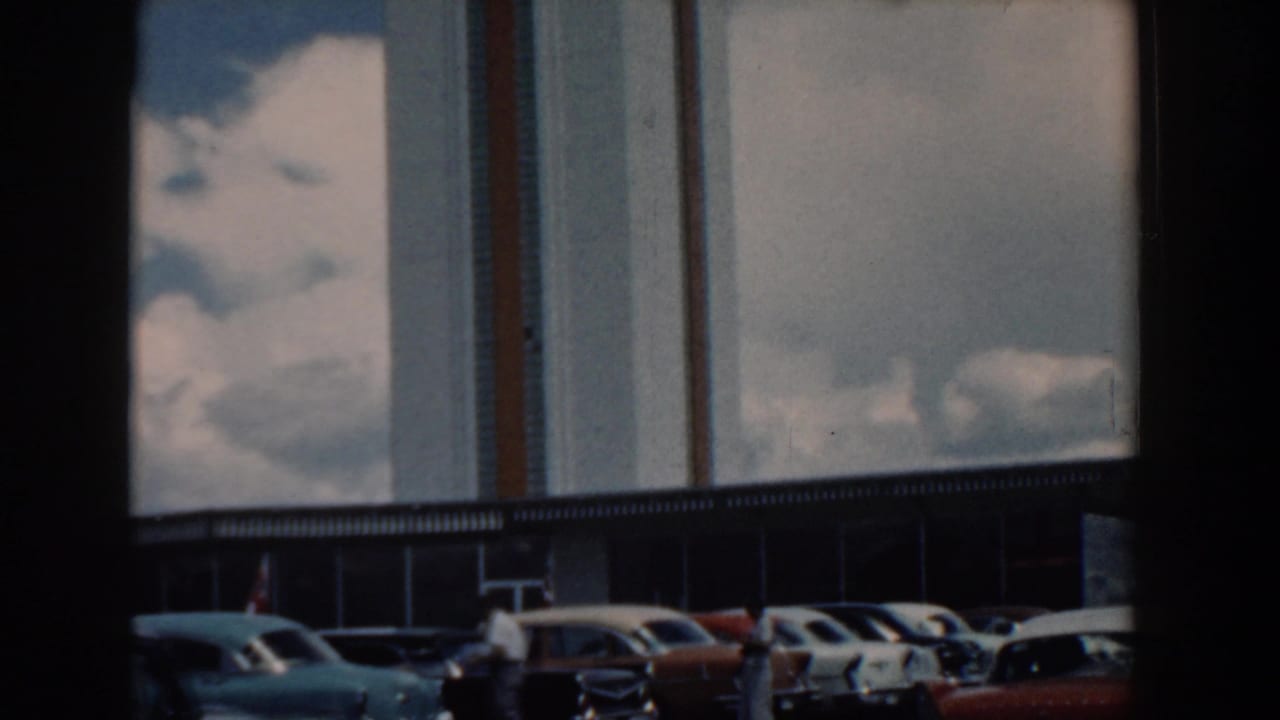 1958 South Carolina 8mm frame showing a reflective modern building facade with several parked cars along the lower edge.