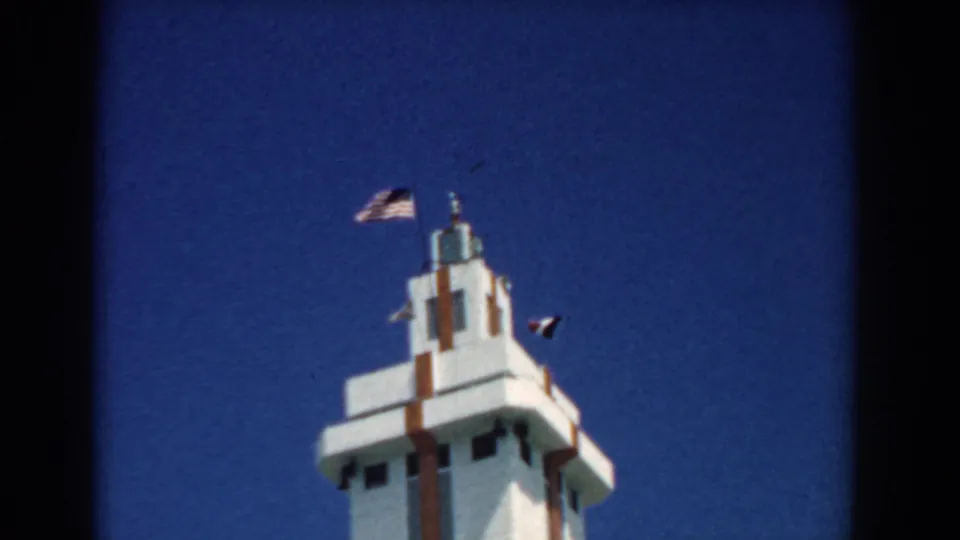 Final 1958 South Carolina frame holding on the white tower, brown trim, American flag, and smaller flag in bright daylight.