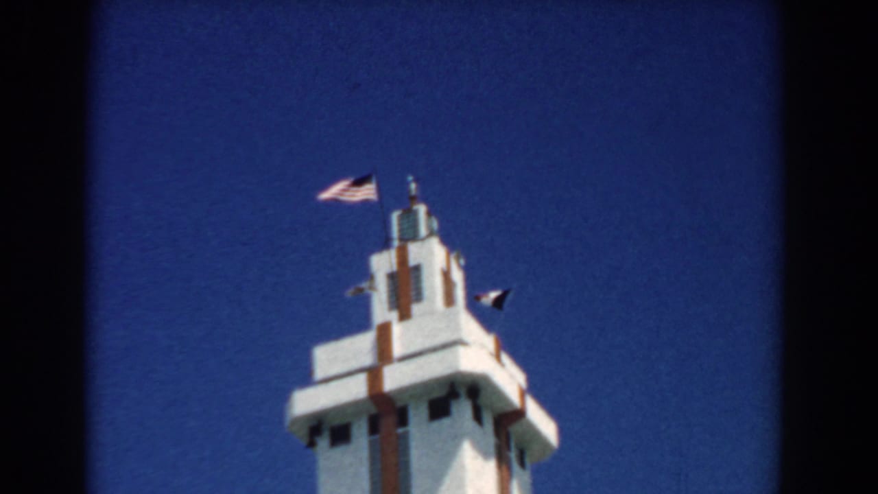 1958 South Carolina 8mm frame showing a white Art Deco-style tower with brown accents and an American flag against a deep blue sky.