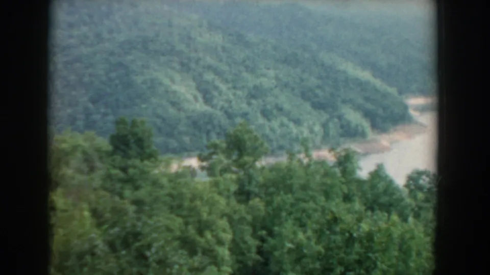 Elevated 1958 South Carolina view of green forested hills and a winding muddy river, filmed in soft 8mm color.