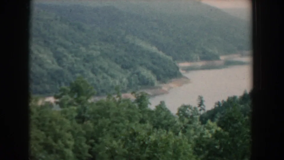 1958 South Carolina 8mm frame showing a muddy river curve below forested hills, with leafy trees filling the lower edge.
