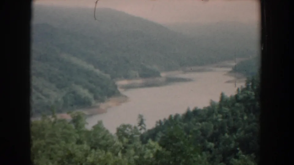 1958 South Carolina 8mm frame showing a soft, slightly faded view of a river bend, wooded hillsides, foreground foliage, and distant hazy terrain.