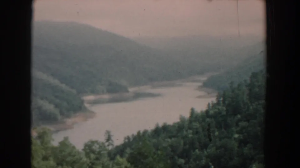 1958 South Carolina 8mm frame showing a winding river bordered by wooded hills under a hazy, overcast sky.
