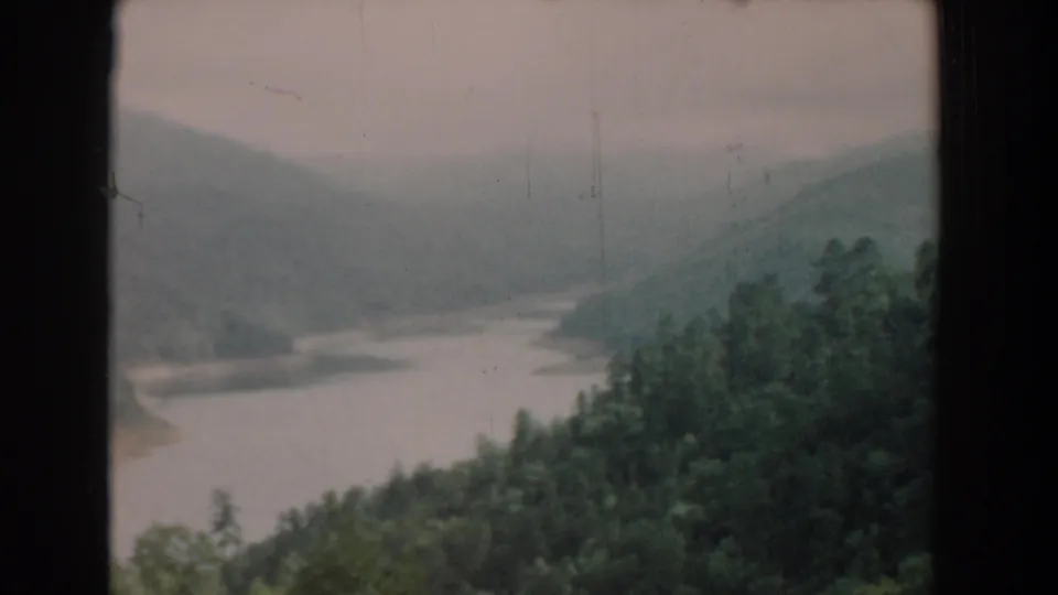 1958 South Carolina home-movie frame with a soft, grainy overlook of a river bordered by dense trees and hazy hills.