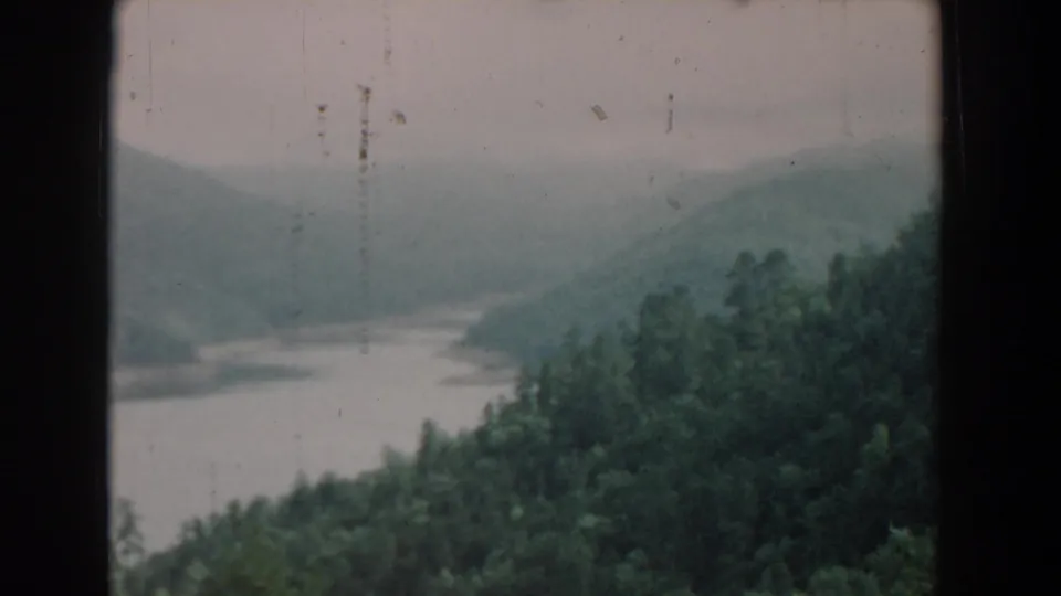 1958 South Carolina 8mm frame showing a wooded riverbank, hazy hill layers, and visible dust marks in the film scan.