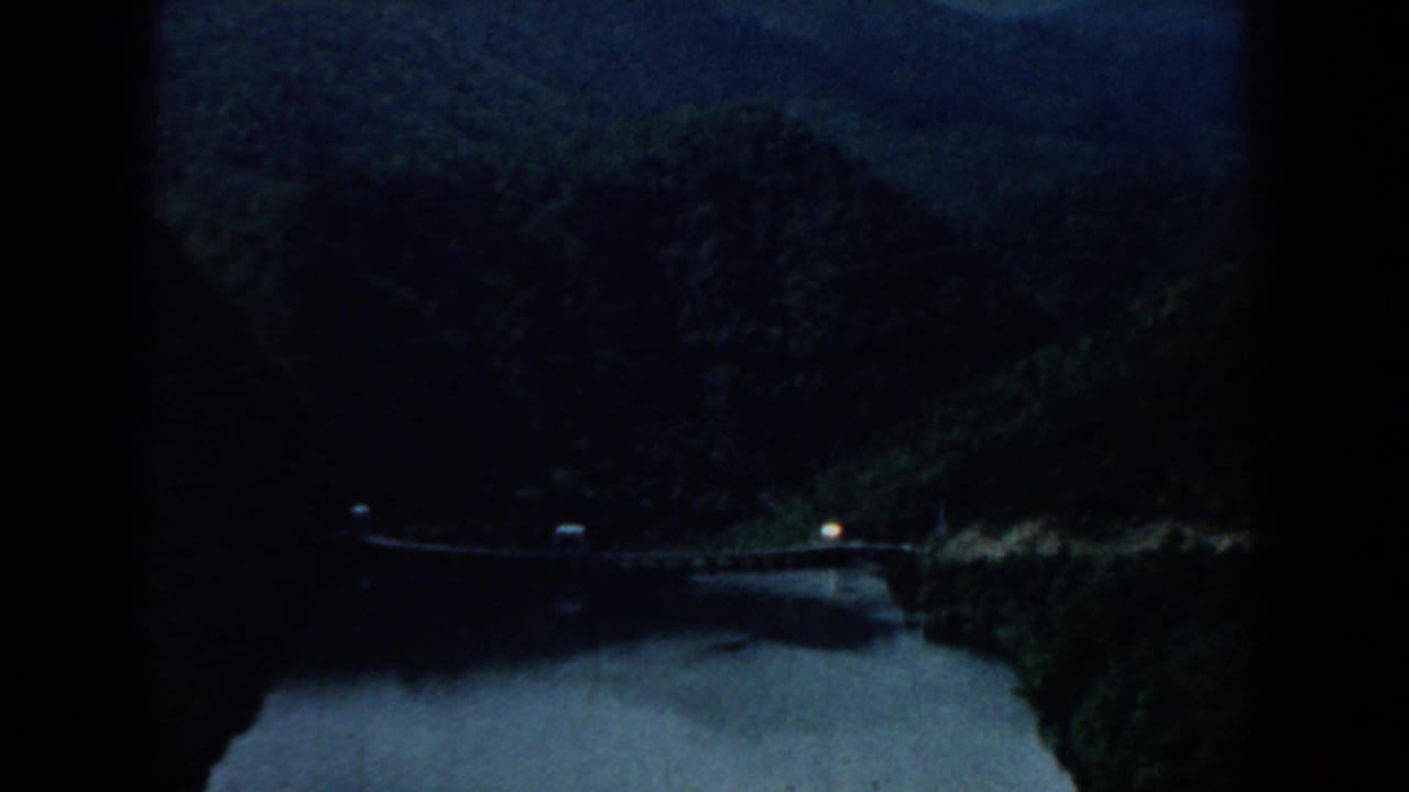 Dark river valley with wooded hills, a bridge edge, and a small light in the distance.