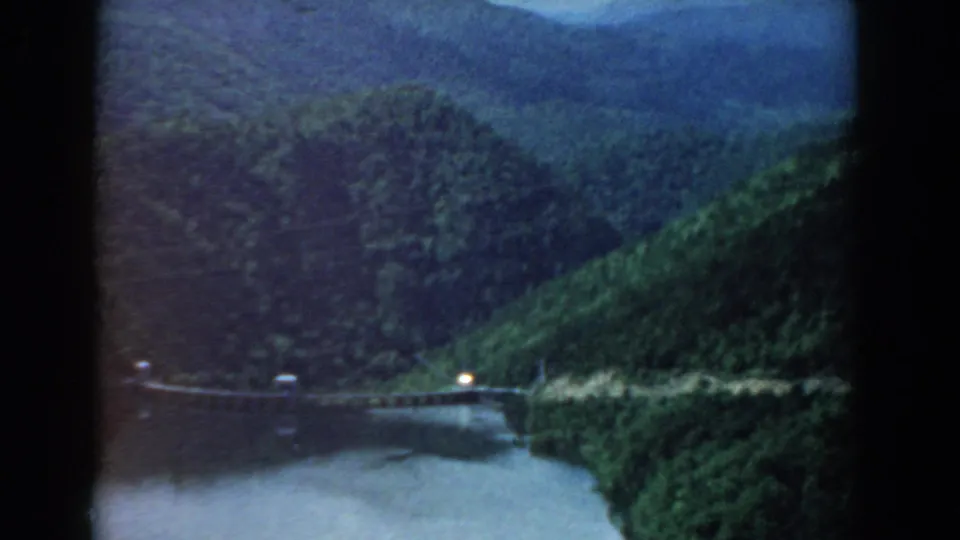 1958 South Carolina 8mm view of a river below dense green slopes, with a small bridge or roadside barrier and one bright light.