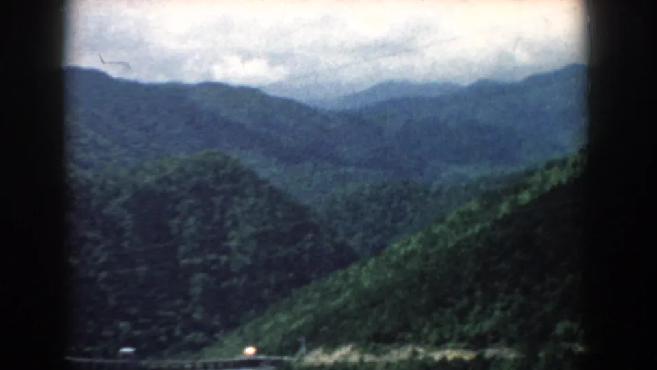 1958 South Carolina 8mm landscape frame showing broad green ridges, a river edge, cloudy sky, and dark film-gate borders.