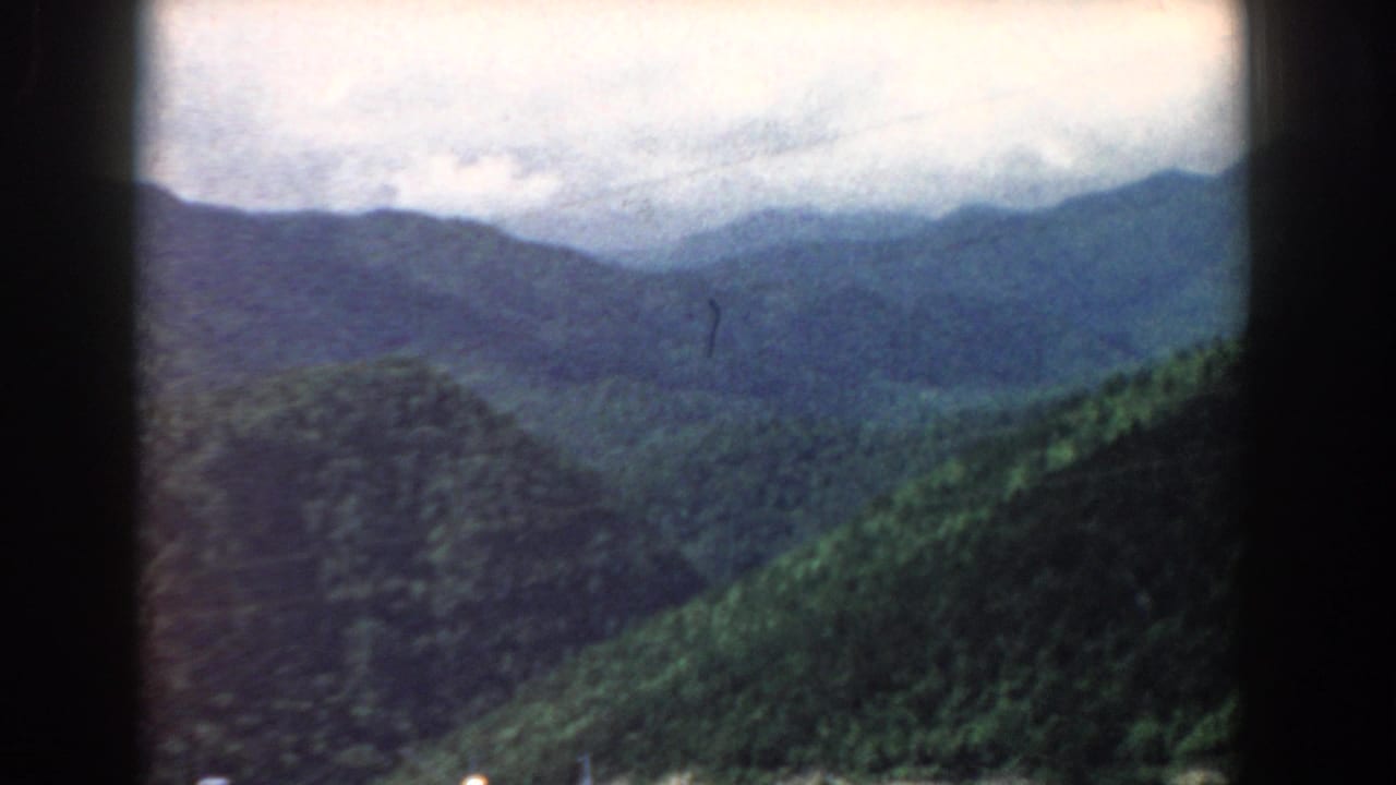 Forested mountain ridges under a cloudy sky with dark 8mm frame borders.