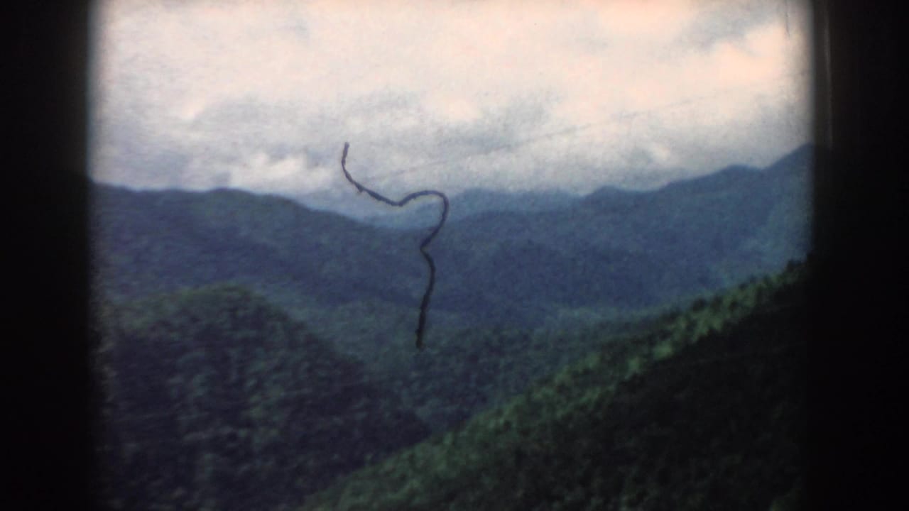 Cloudy mountain view with green ridges and a dark hair or dust mark on the film.