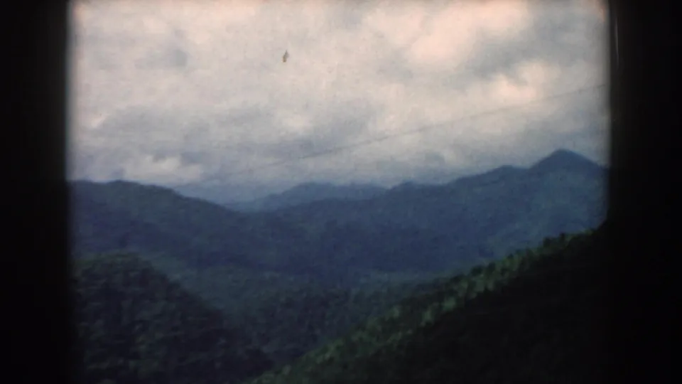 1958 South Carolina 8mm frame showing distant blue-green peaks, a darker foreground ridge, and heavy clouds across the sky.