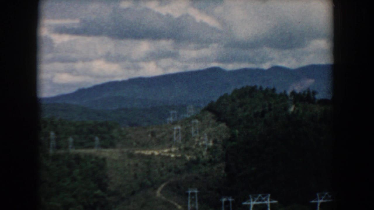 Forested hills beneath a cloudy sky with utility towers crossing the valley.