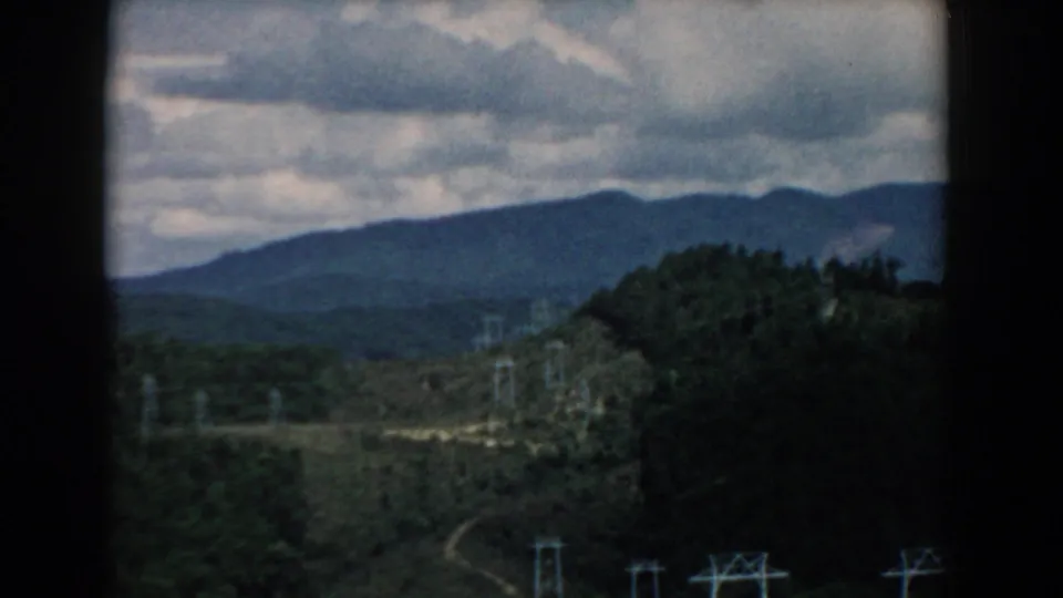 1958 South Carolina 8mm frame showing layered wooded hills, a cloudy sky, and electrical transmission towers in the valley.