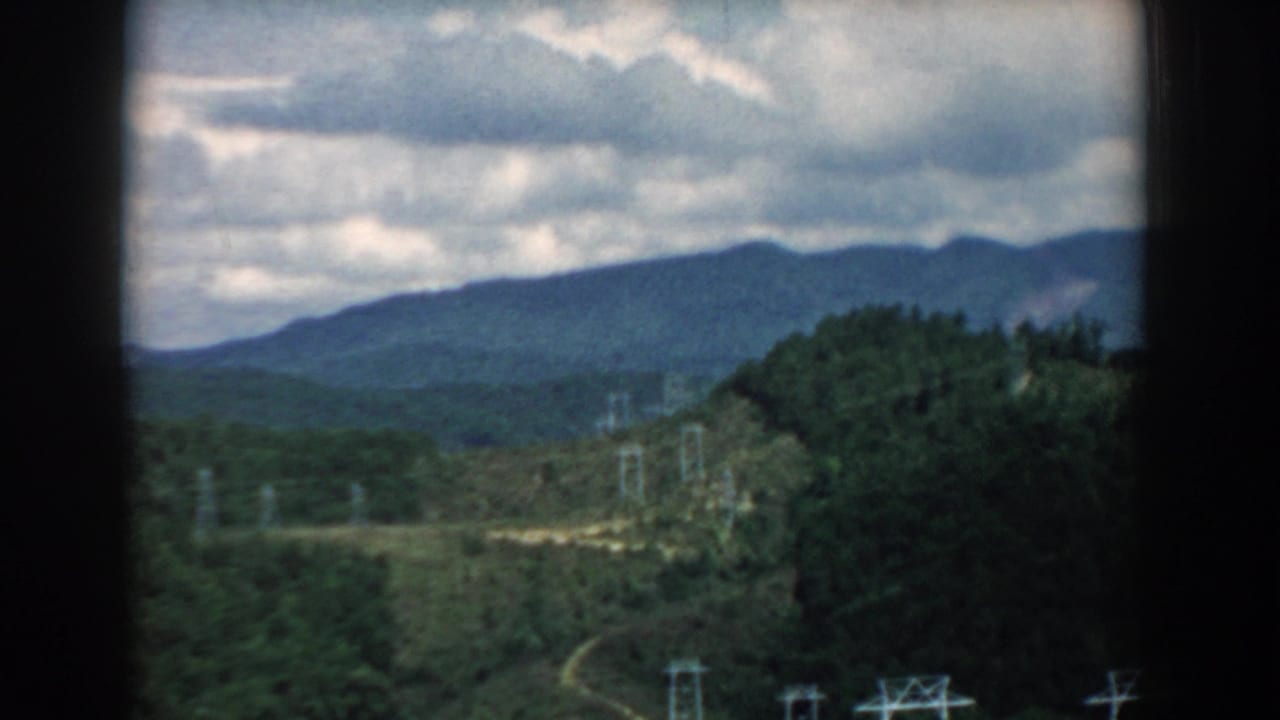 Distant blue-green hills, wooded foreground, and transmission towers under heavy clouds.
