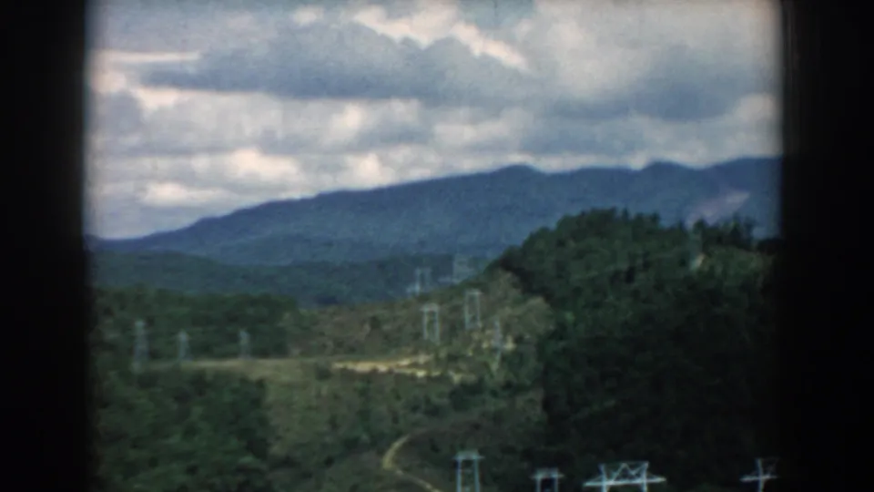 1958 South Carolina landscape view with layered hills, dense trees, and utility towers visible beneath a dramatic cloudy sky.