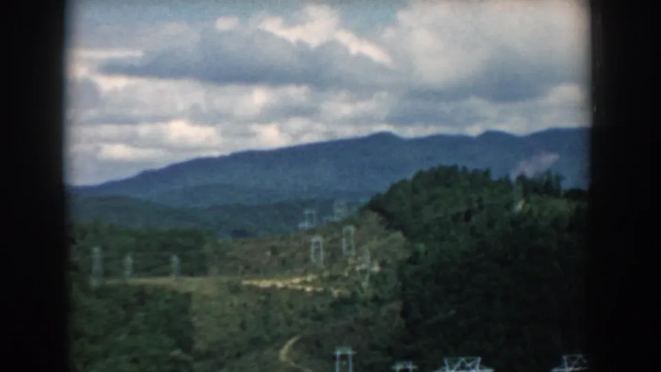 1958 South Carolina 8mm frame showing a forested valley, electrical transmission towers, and a blue ridge under cloud cover.