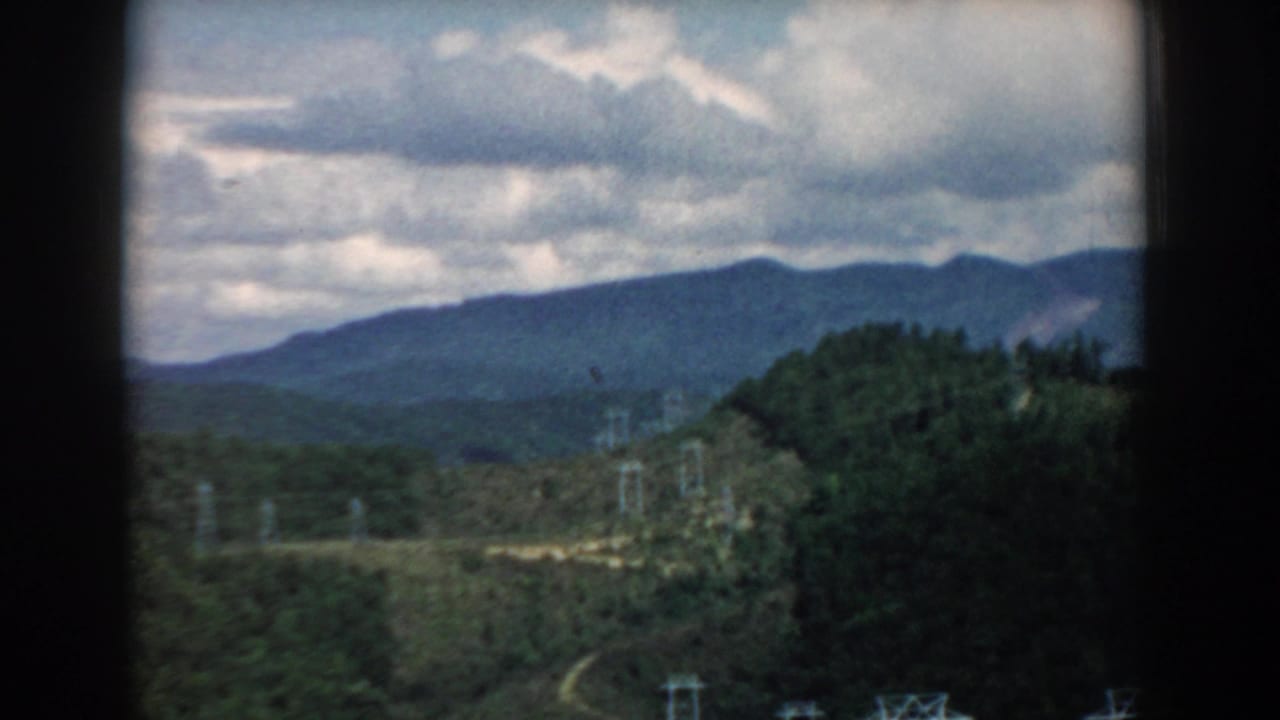 1958 South Carolina 8mm frame showing rolling hills, distant blue mountains, cloudy sky, and utility lines in a scenic overlook view.