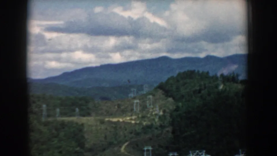 1958 South Carolina 8mm frame showing rolling hills, distant blue mountains, cloudy sky, and utility lines in a scenic overlook view.