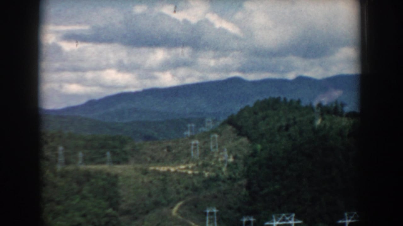 Mountain vista with layered hills, cloudy sky, and utility towers near the center of the frame.