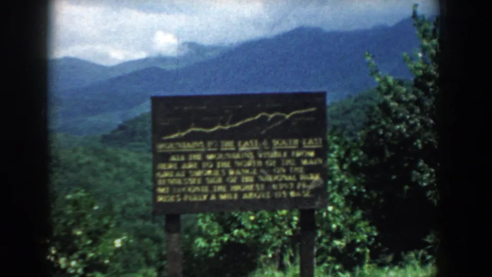 1958 South Carolina 8mm frame showing a brown and yellow tourist sign at a mountain overlook with ridges behind it.