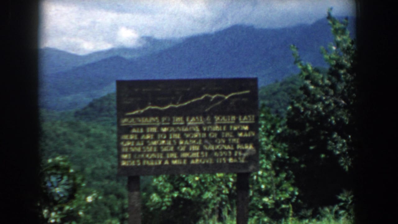 Dark overlook sign in front of green hills and distant blue mountains.