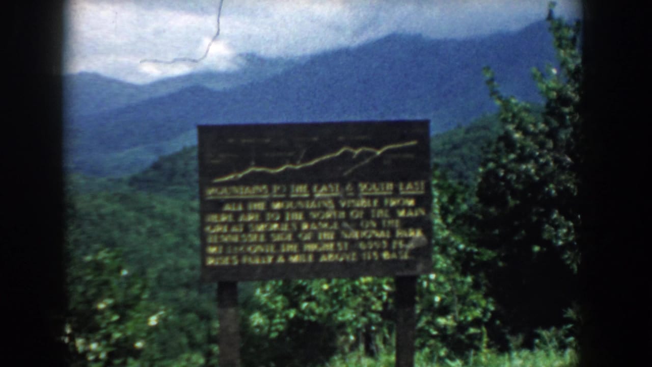 Overlook sign centered against forested ridges and cloudy mountain sky.