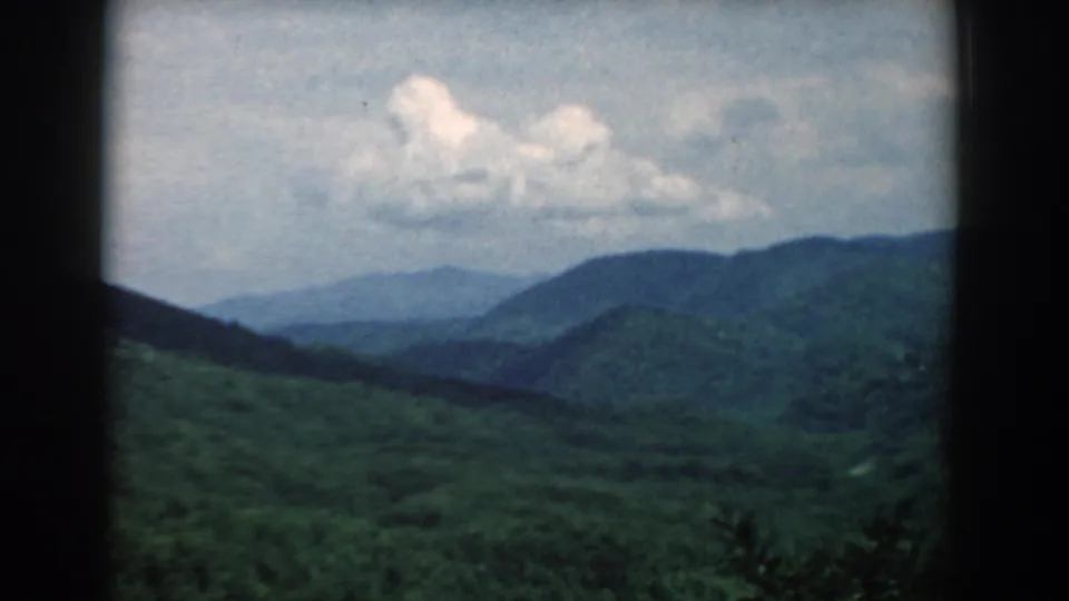1958 8mm landscape view across rolling South Carolina forest and layered blue mountain ridges.