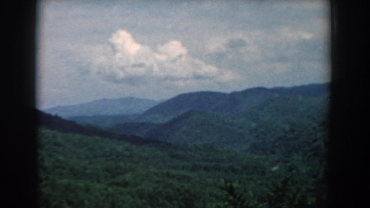 1958 South Carolina 8mm frame showing layered green mountain ridges, a hazy valley, and cloud cover within dark film borders.