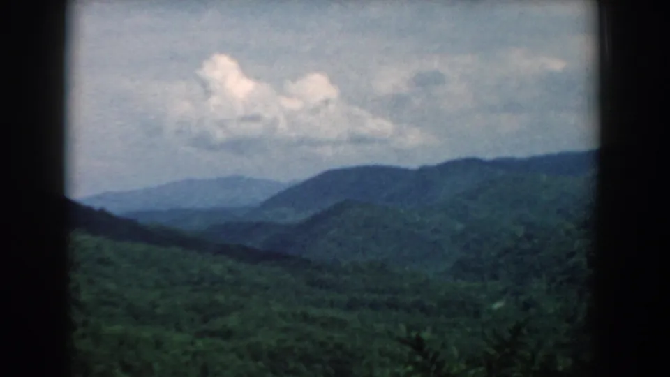 1958 South Carolina 8mm frame showing layered green mountain ridges, a hazy valley, and cloud cover within dark film borders.