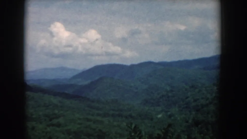1958 South Carolina scenic 8mm view with blue-green mountain layers, a pale cloudy sky, and soft archival film texture.