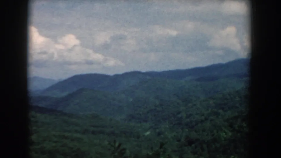 1958 South Carolina home-movie frame showing wooded mountain slopes and distant ridges beneath a bright, clouded sky.