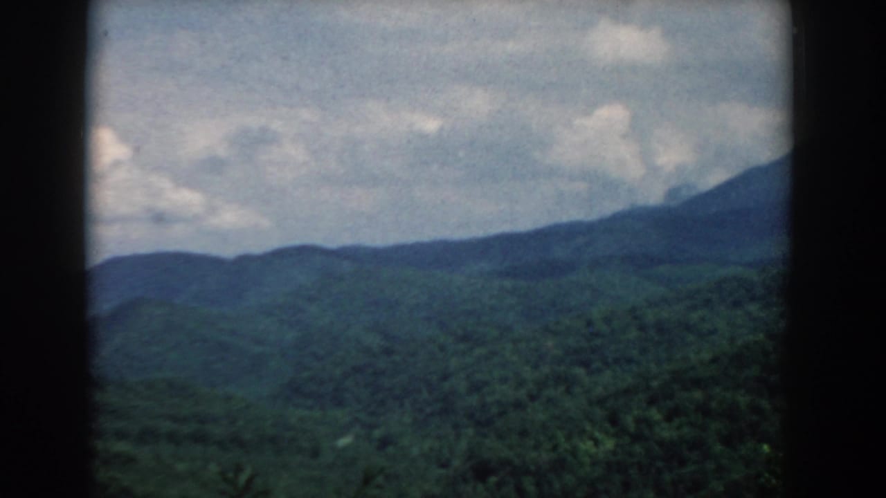 Forested mountain ridges under a partly cloudy sky with dark vertical frame borders.
