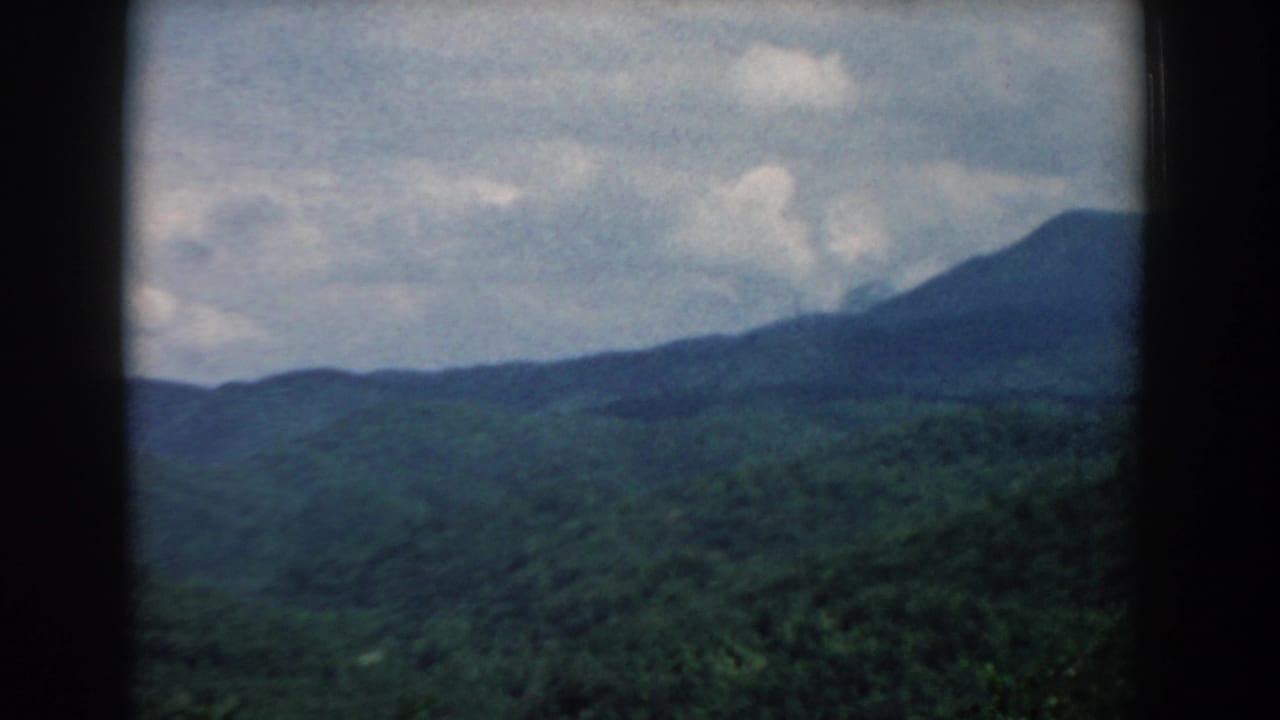 Mid-century 8mm view of South Carolina mountain terrain, with wooded ridges and soft cloud cover framed by dark edges.