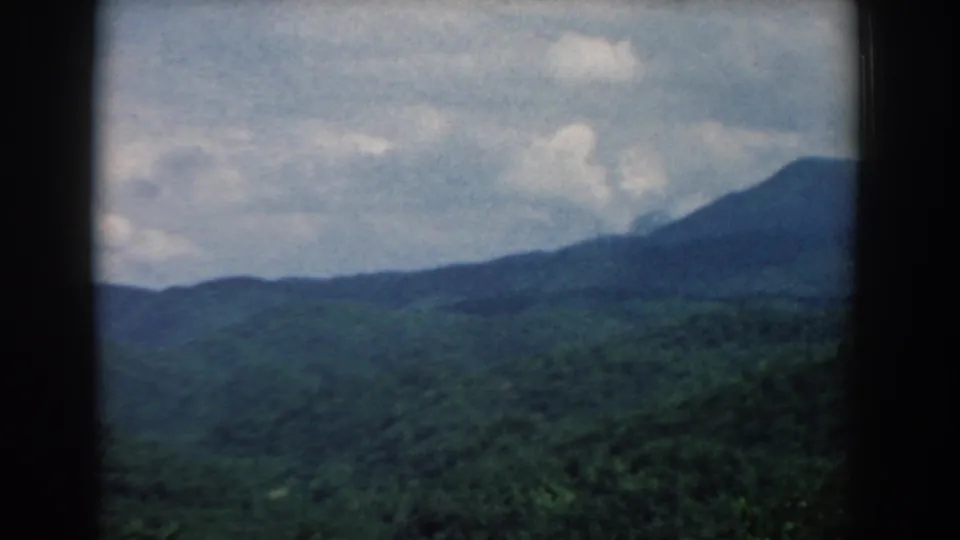 Mid-century 8mm view of South Carolina mountain terrain, with wooded ridges and soft cloud cover framed by dark edges.