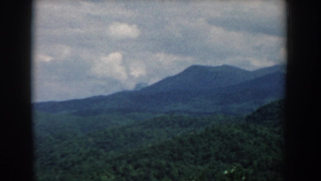 Forested hills and a distant ridge under a cloudy sky, seen through dark film borders.