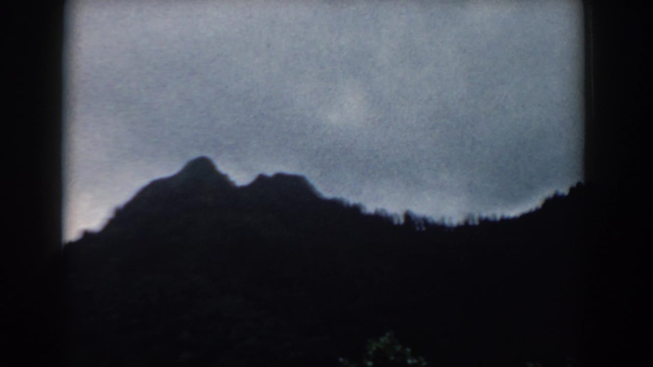 1958 South Carolina 8mm frame of a shadowed ridgeline and treetops under a gray-blue overcast sky.