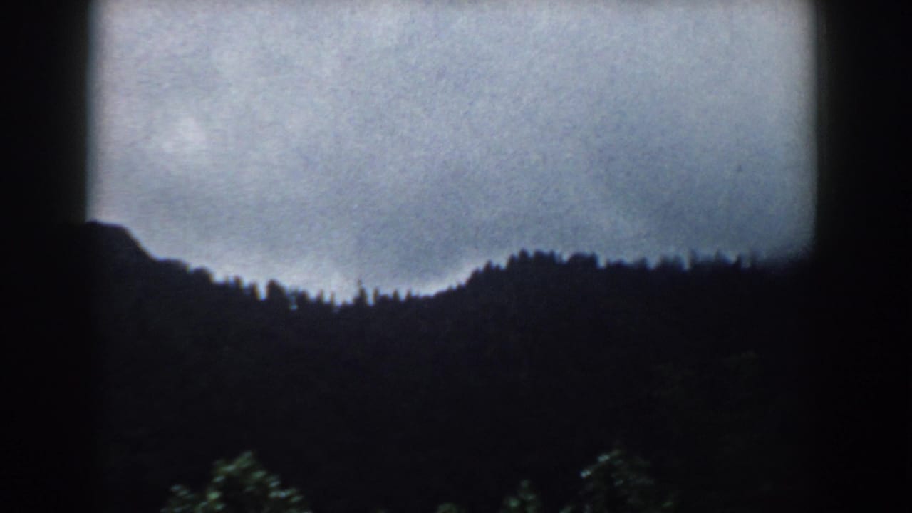 Dark wooded hills under a gray overcast sky with rounded 8mm frame edges.