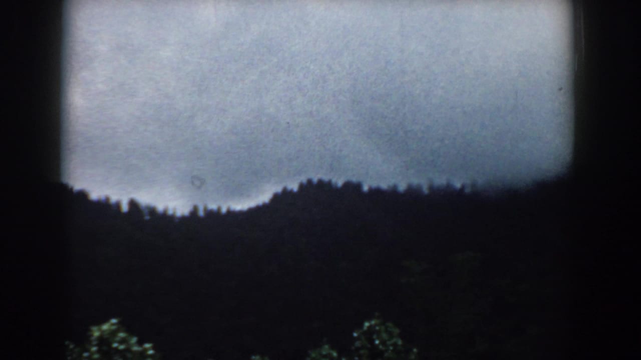 Overcast sky above a dark forest ridge, framed by black film borders.