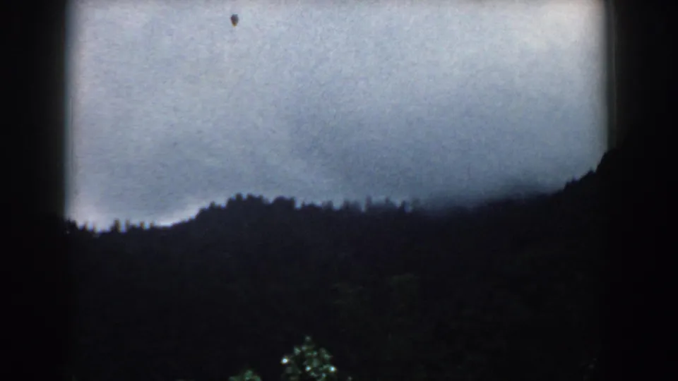 1958 South Carolina 8mm frame with dark hills, low treeline, cloudy sky, and a small film speck near the upper area.