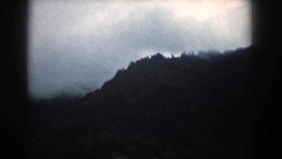 A late frame from the 1958 South Carolina 8mm clip shows low clouds crossing above a dark, forested hillside.